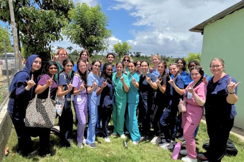 Dr. Cayla Lanier and Honors students pose in scrubs and hold up the Go Bulls hand sign in the Dominican Republic