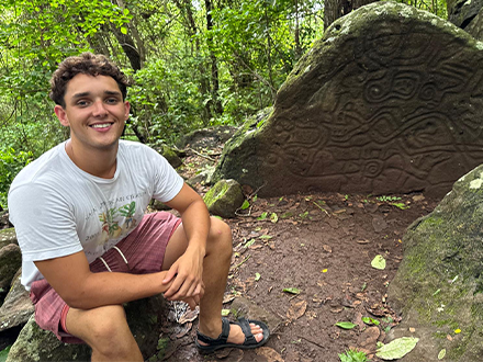 Jackson Anderson sitting beside a large rock that has grooves in it