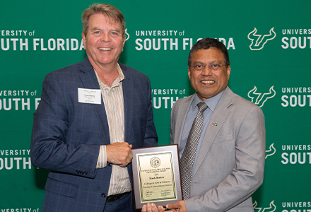 Two people holding awards with green USF backdrop