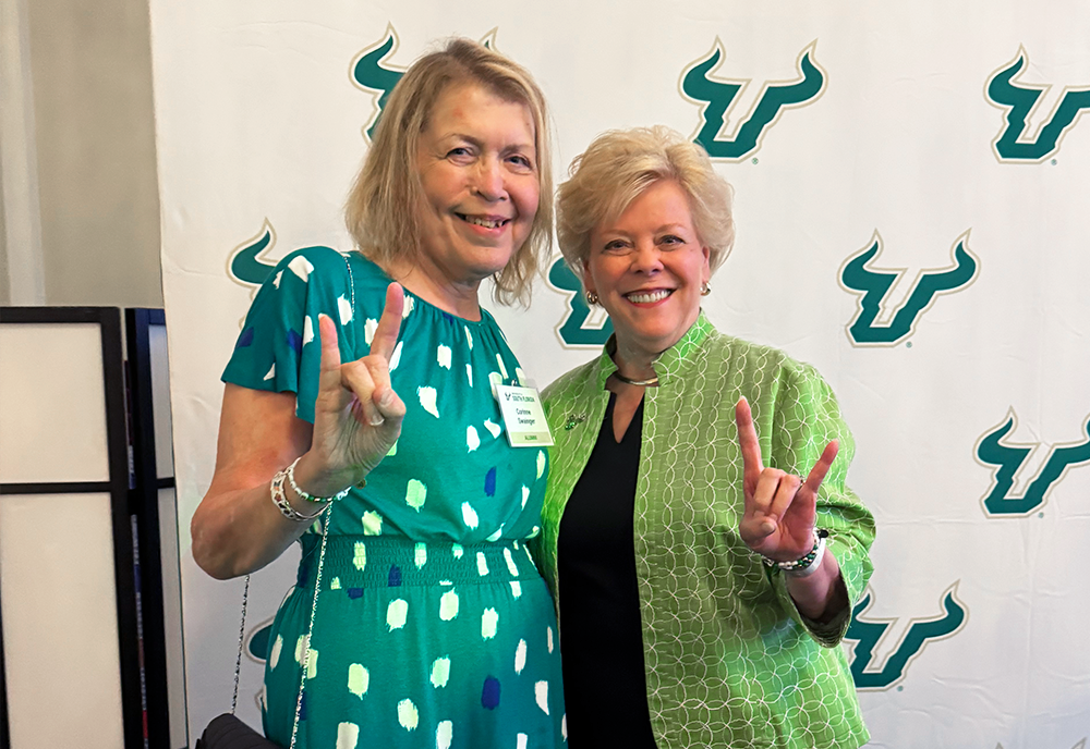 Corinne and USF President Rhea Law standing together smiling raising the bulls "sign"
