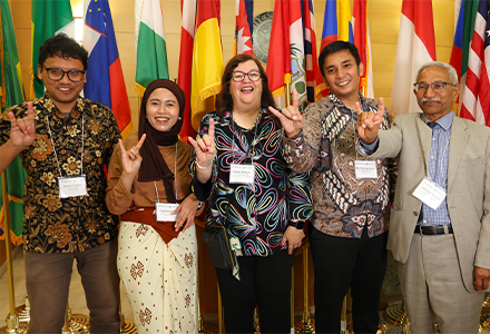 Group of people smiling and holding up bulls signs, standing in front of flags from all over the world