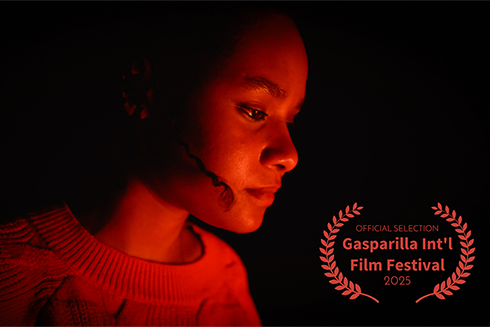 A girl is aglow in red light and looking down. Darkness is behind her.