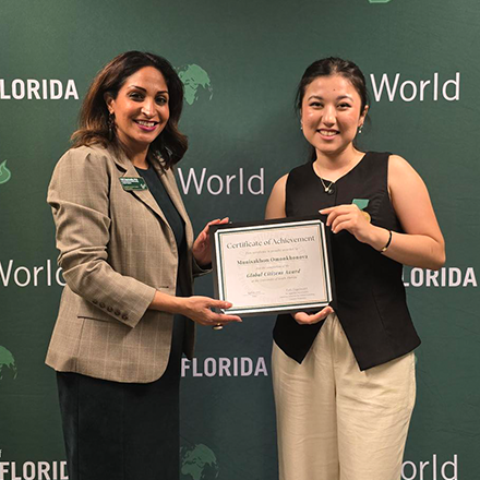 Two people smiling and holding an award in front of a green background that says "USF World"
