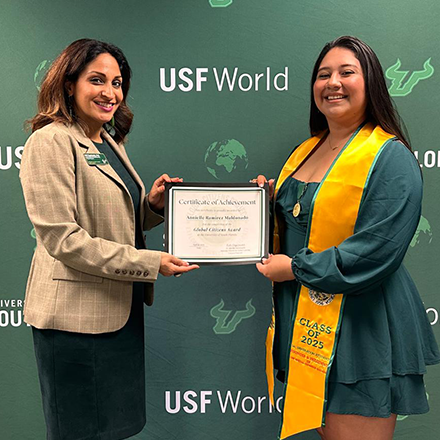 Two people smiling and holding an award in front of a green background that says "USF World"