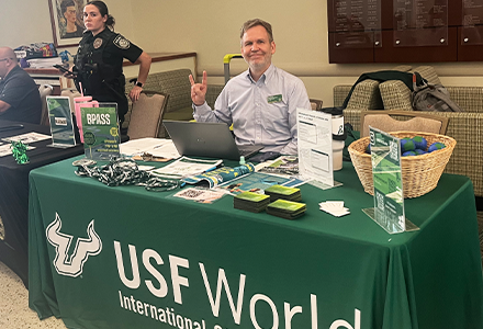 USF staff sitting at USF World booth and holding up the bulls sign with hand