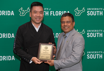 Two people holding awards with green USF backdrop