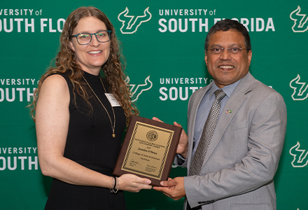 Two people holding awards with green USF backdrop