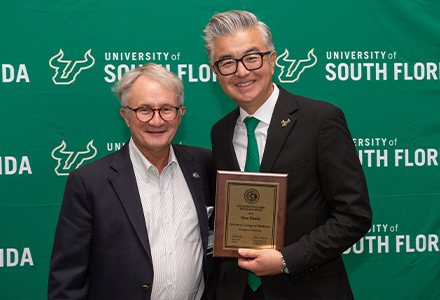 Two people holding awards with green USF backdrop