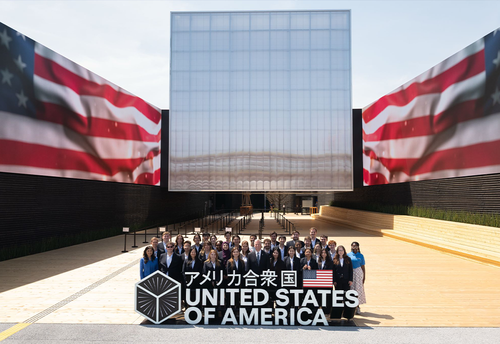A group of people standing outside of the world expo building and behind a large sign that says "United States of America"