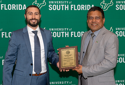 Two people holding awards with green USF backdrop
