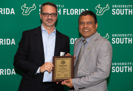 Two people holding awards with green USF backdrop