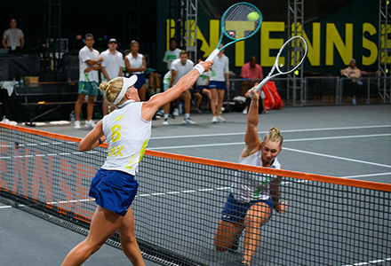 two tennis players reaching for tennis ball over net