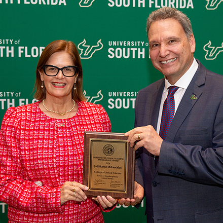 An awardee smiling holding a plaque with the USF President Limayem