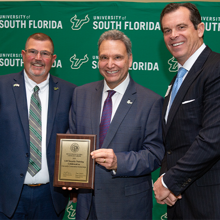 An awardee smiling holding a plaque with the USF President Limayem