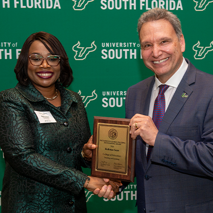 An awardee smiling holding a plaque with the USF President Limayem