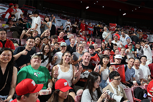 People in a stadium raising their hands and smiling