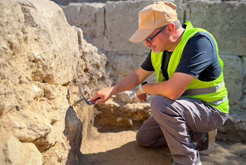 Davide Tanasi excavates a stone wall at the Roman Villa del Tellaro in Sicily.
