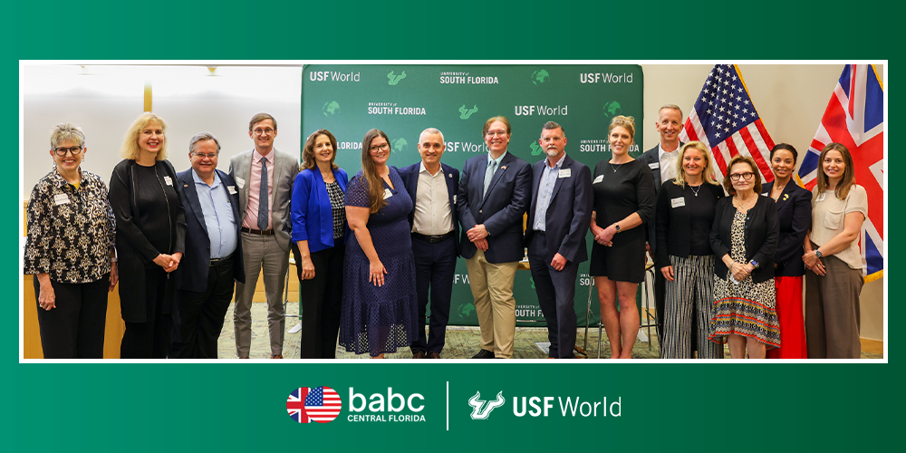 Group of people smiling in front of USF World step and repeat backdrop with BABC and USF World logo underneath on a green background