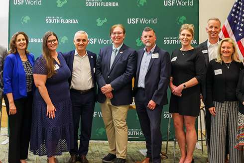 Group of people smiling in front of USF World step and repeat backdrop with BABC and USF World logo underneath on a green background