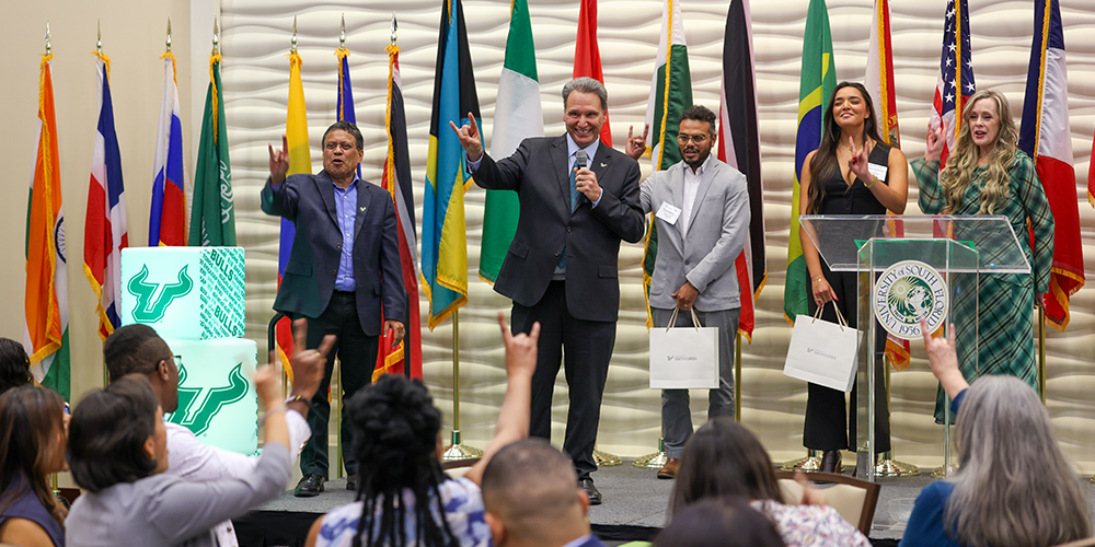 A group of people smiling with the USF President, provost and VP of USF World and holding up hands in a "go bulls" symbol