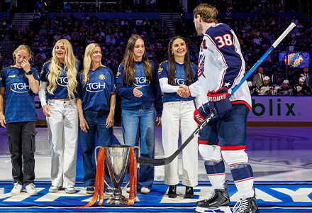 Listro with team on hockey field, shaking a hockey player's hand