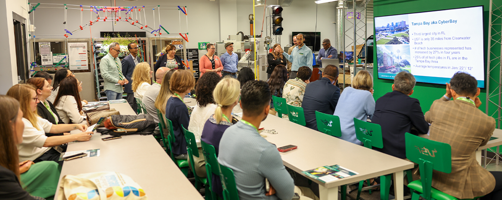 A group of people sitting in green metal chairs with the USF logo carved in the backs--a faculty member is speaking to the group