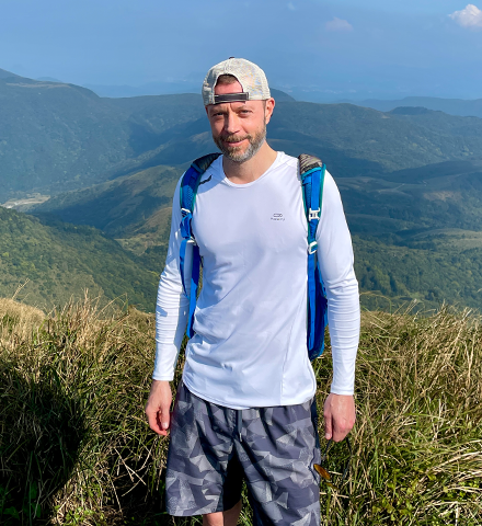 Tyler smiling in a blue shirt with mountains in the background