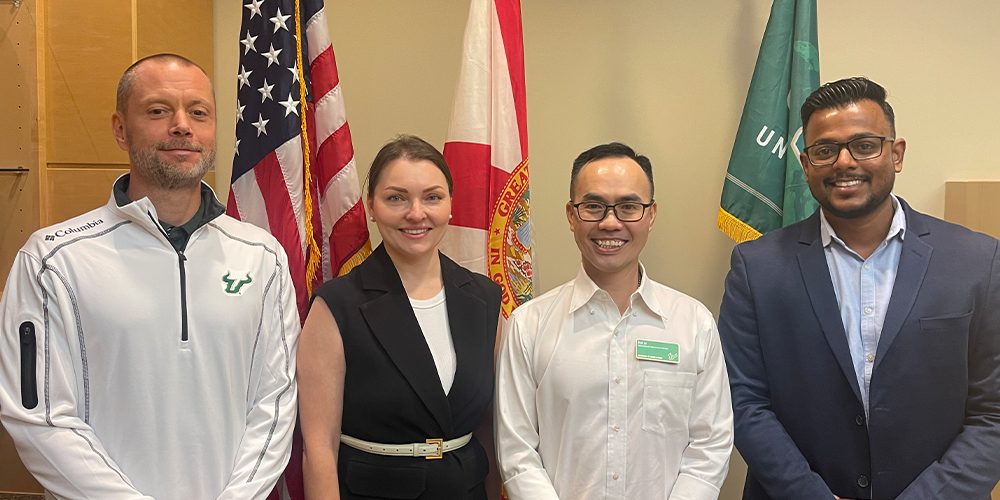 USF staff and Tyler stand together in front of the U.S., FL, and USF flags