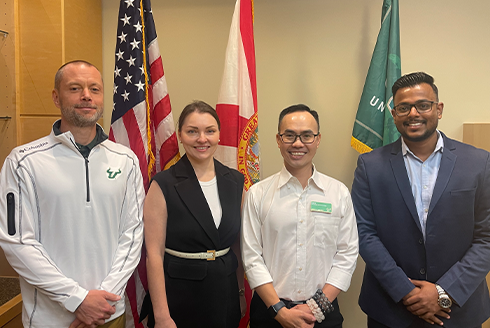 USF staff and Tyler stand together in front of the U.S., FL, and USF flags