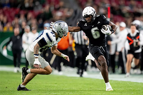 two football players in the field, one holding a football and is holding up a hand toward the opponent