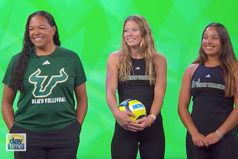 Three people smiling wearing USF shirts and the middle person holding a volleyball with a green background